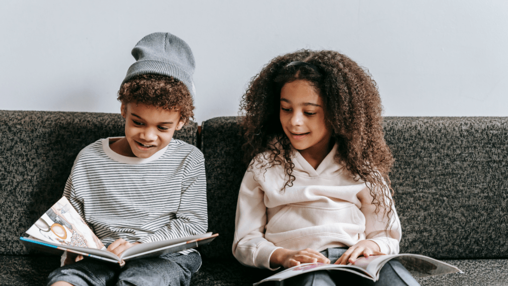 two children sitting on a couch reading books