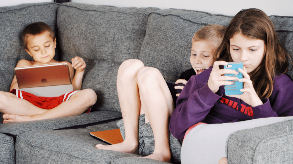 children sitting on a couch with their cell phones