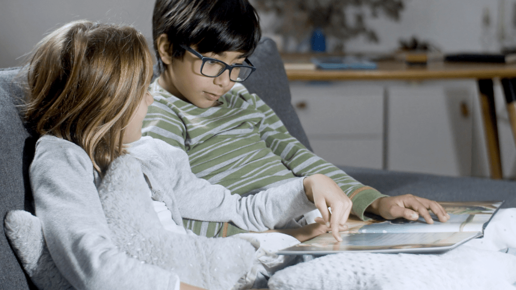 two children sitting on a couch reading books